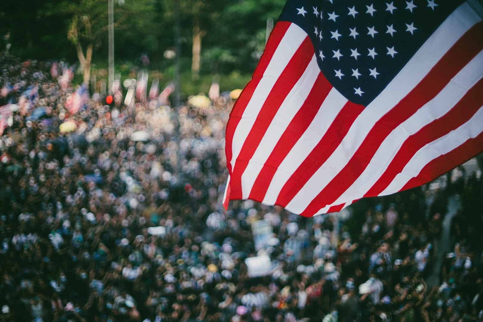 Image of the USA flag in-front of a dense crowd signifying community